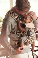 BabyBjörn Baby Carrier One in cotton beige/leopard, side-worn view supports hands-free tasks.