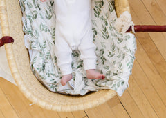 Copper Pearl Fern swaddle blanket baby-in-onesie shot shows versatile newborn use.
