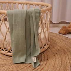 Huxie knitted baby blanket Roman Green in crib for daytime comfort.
