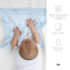 Little Giraffe Blanky blue satin-trim blanket draped over crib edge for nap-time comfort
