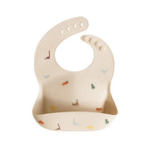 Mushie silicone bib dinosaurs neck-fastener closeup for adjustable fit and mess control.