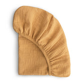 Mushie extra-soft muslin fitted crib sheet in Fall Yellow on a crib mattress for cozy, breathable sleep.