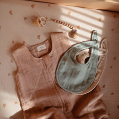 Mushie muslin bib designed for ages 0-24 months with adjustable fit.