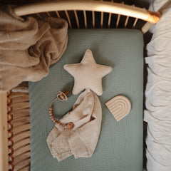 Mushie roman green crib sheet folded to show deep pocket fit and snug elastic.