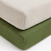 Pet Rejoir muslin fitted crib sheets in olive green and beige on a crib, cozy sleep space.