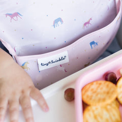 Tiny Twinkle wipeable bib capturing crumbs with deep catch pocket.