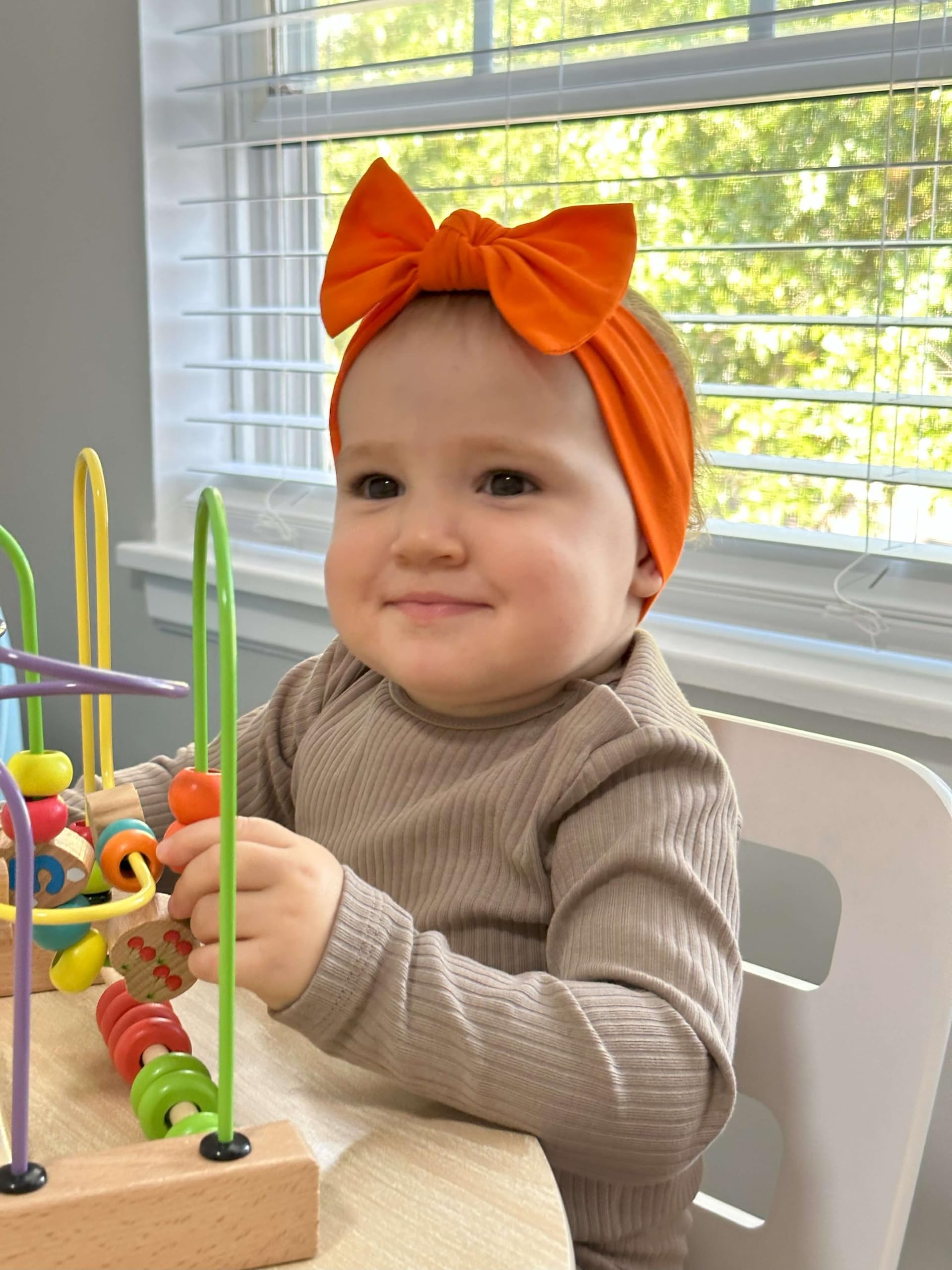 BABYGIZ orange-bow headband being adjusted to show flexible sizing up to 1 year.