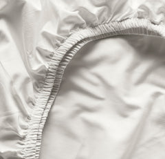 Boll & Branch Signature crib sheet secure-fit elastic band demonstrates snug bedding for standard crib.
