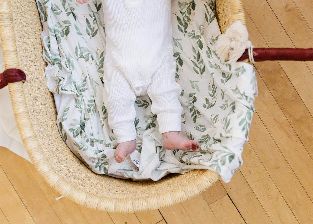 Copper Pearl Fern swaddle blanket baby-in-onesie shot shows versatile newborn use.