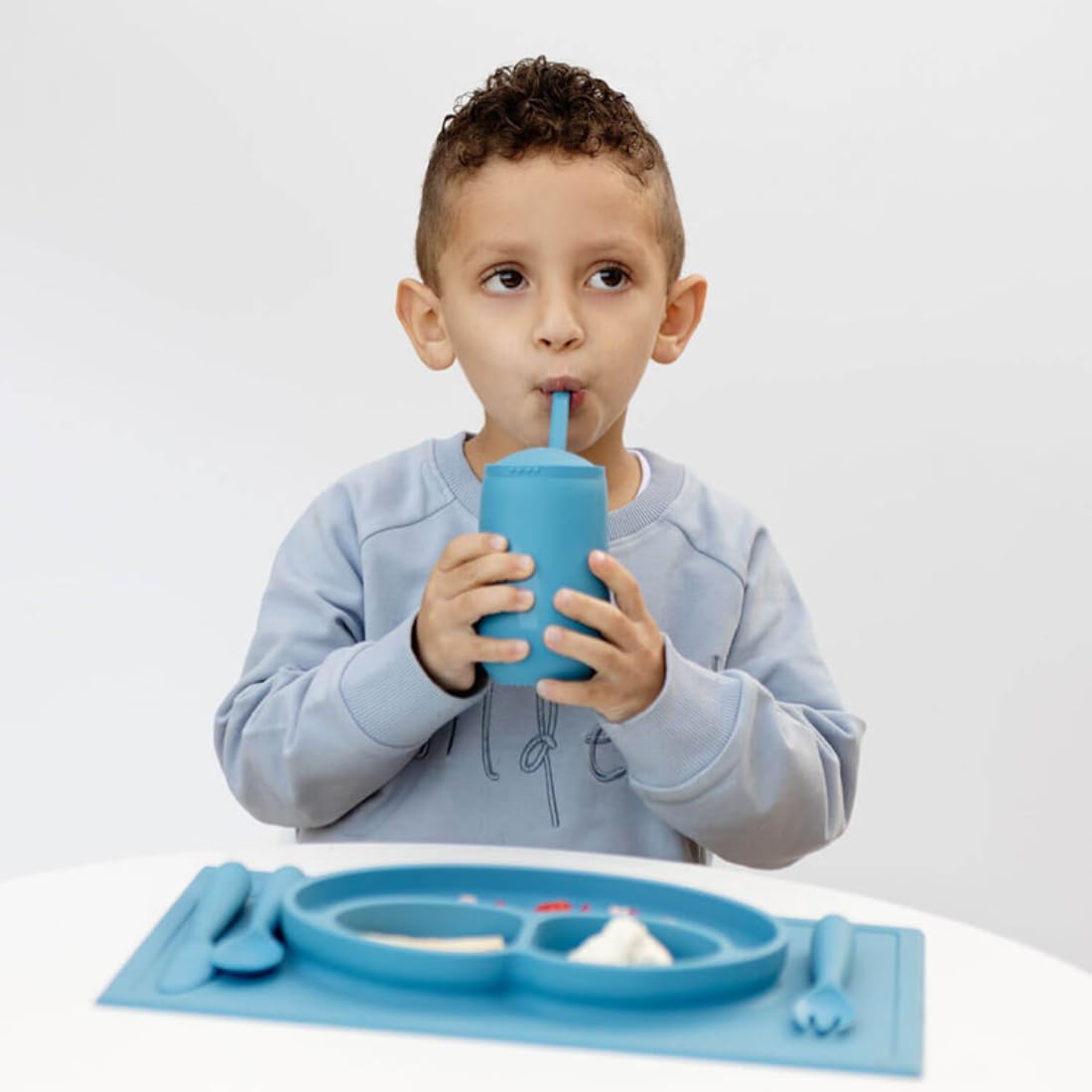 ezpz Happy Cup + Straw System blue child using the cup confidently