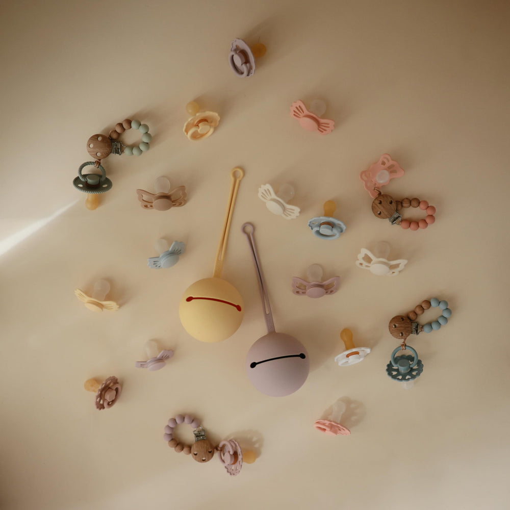 FRIGG Butterfly click-lock system image shows secure pacifier attachment