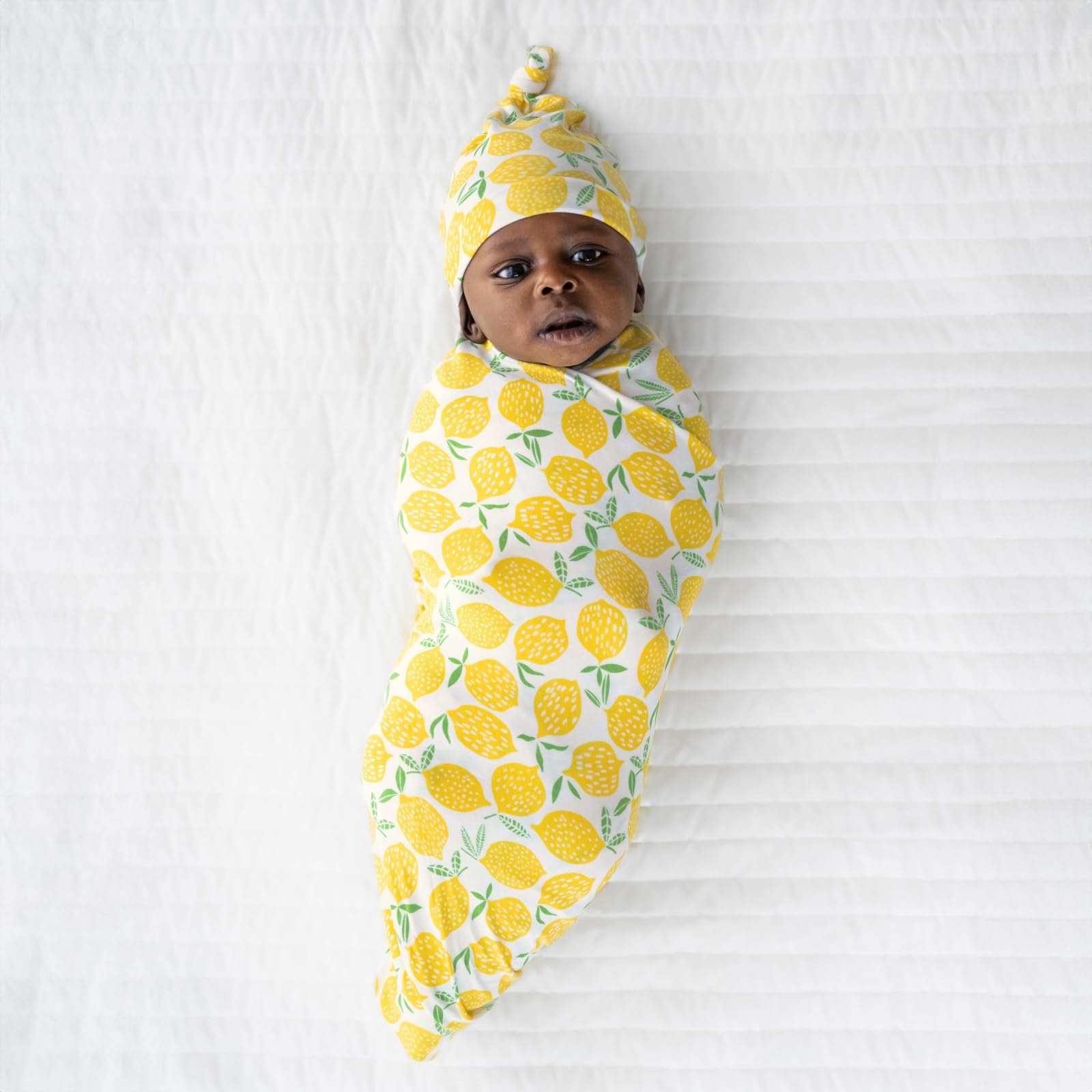 Little Sleepies lemon swaddle set on bed shows versatile, comfy sleep and travel essential.