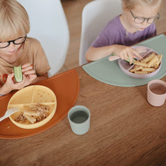 Mushie cups held by a hand show kid-friendly size and ergonomic grip.