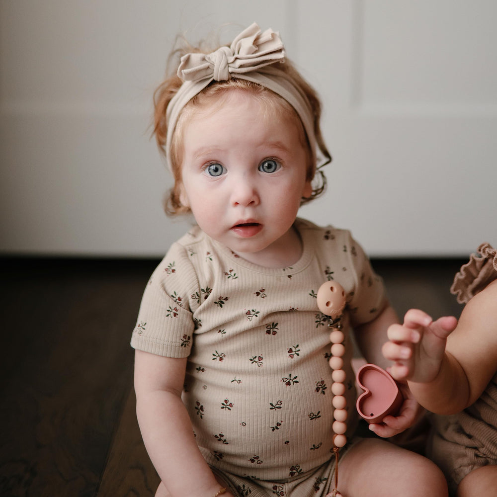 Mushie Hera pacifier clip in soft color palette complements outfits.