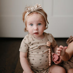 Mushie Hera pacifier clip in soft color palette complements outfits.