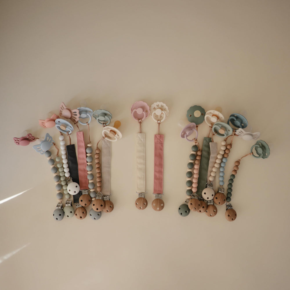 Mushie linen pacifier clip Dusty Rose with faux wood clasp for secure pacifier hold.