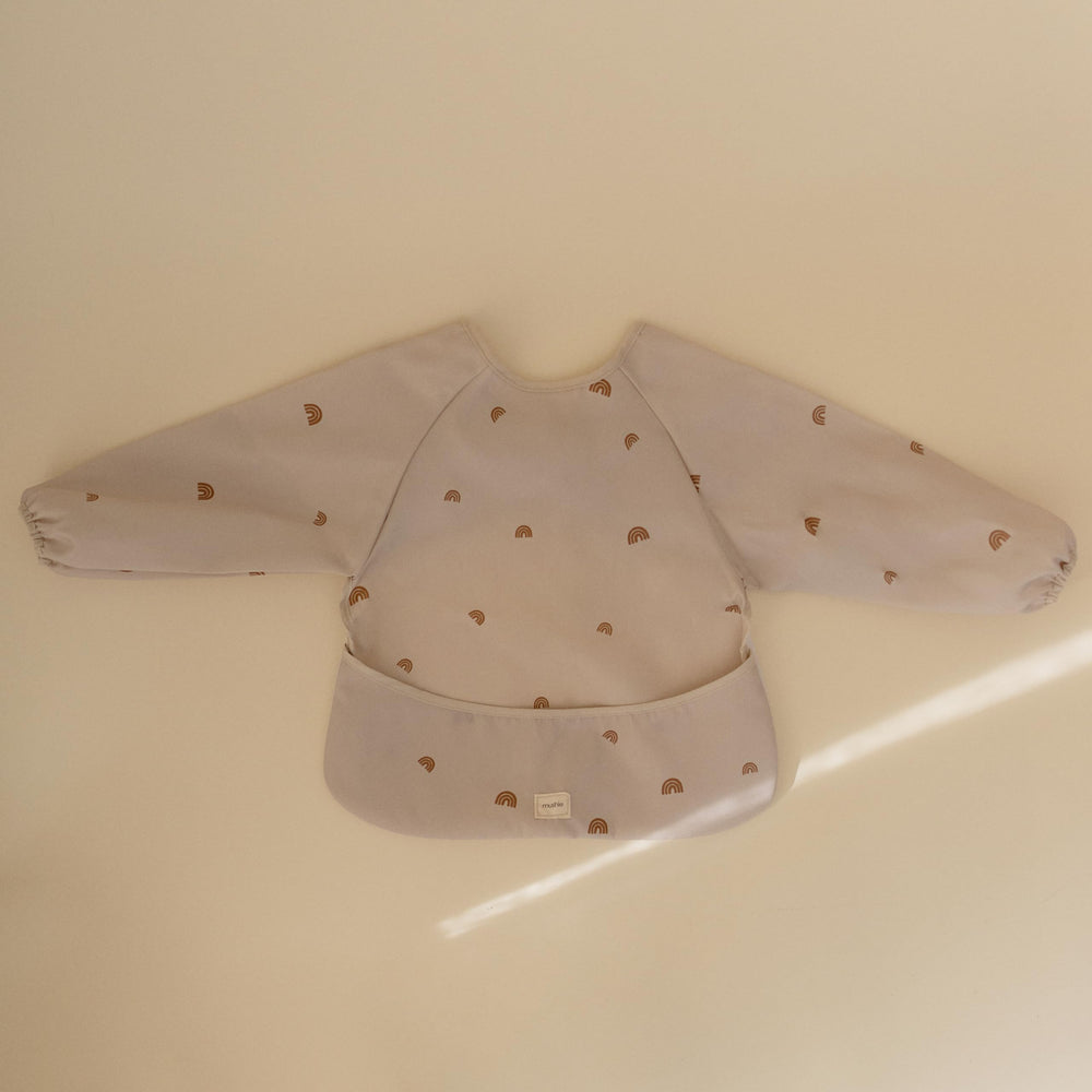 Mushie Rainbows long sleeve bib highlights the wide pocket catching crumbs at feeding time.