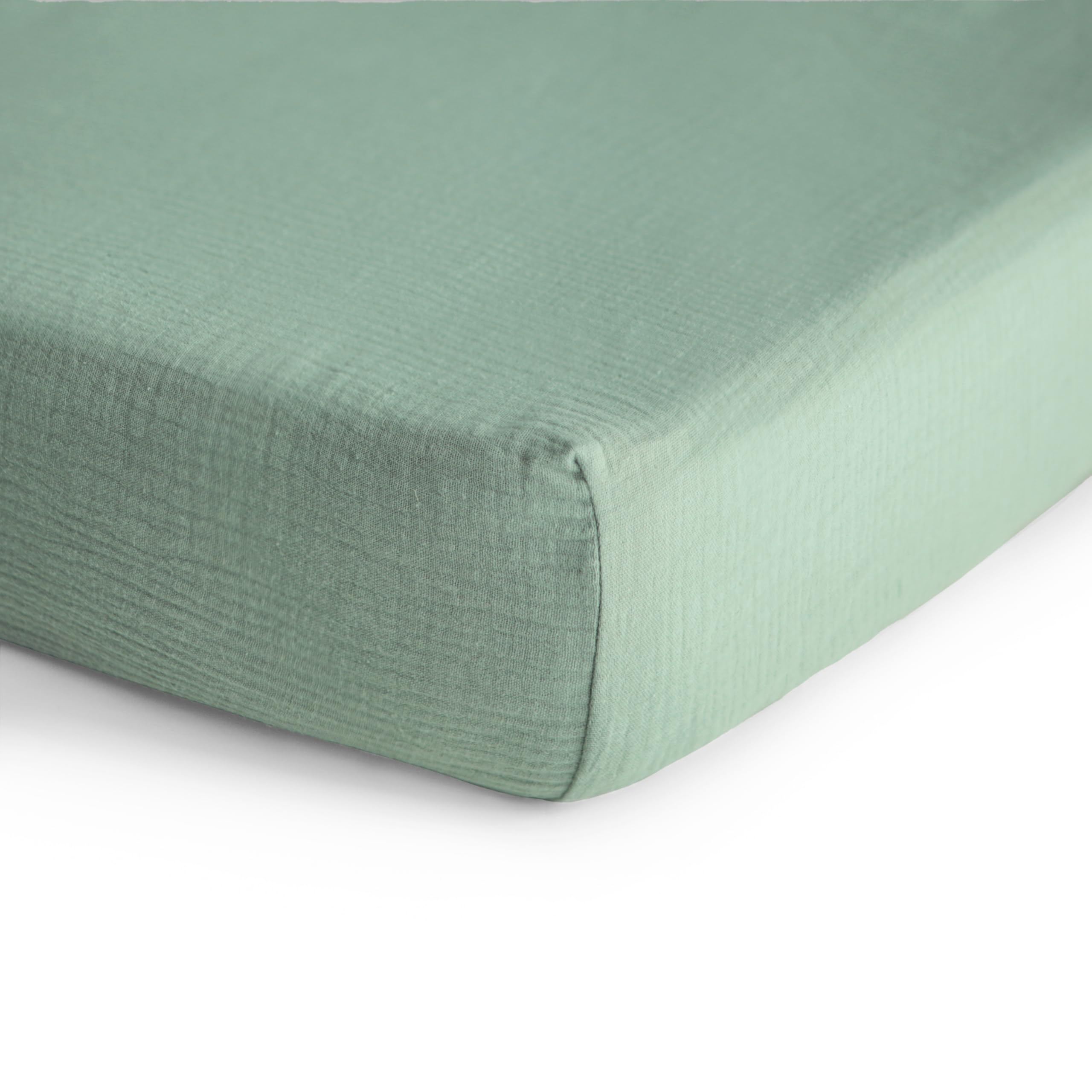 Mushie muslin crib sheet on mattress close-up in Roman Green with elastic edge.