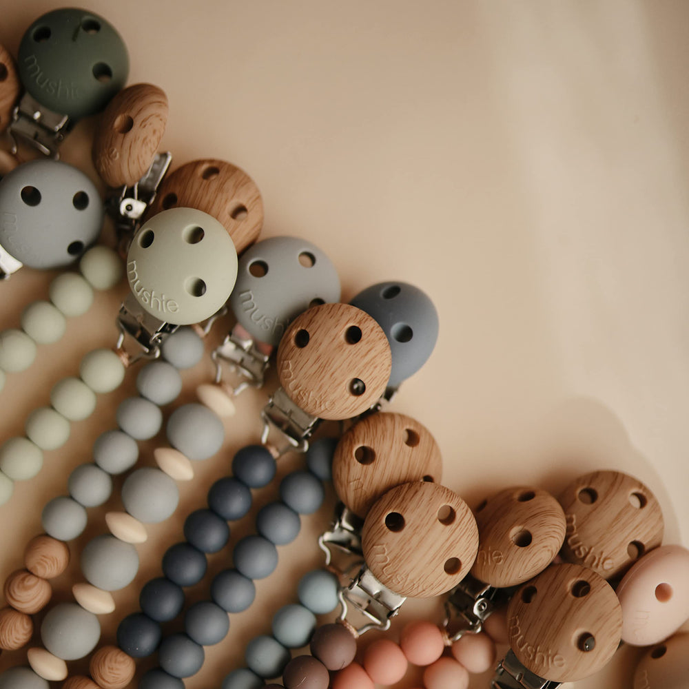 Mushie on-the-go clip attached to stroller demonstrates secure pacifier management