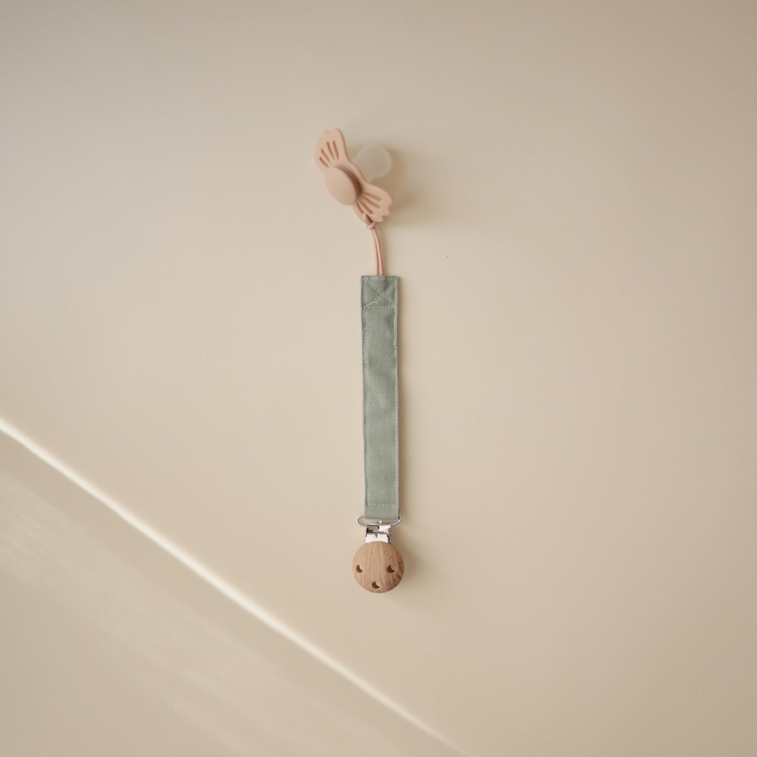 Mushie pacifier clip soft fabric strap on olive demonstrates gentle touch for baby comfort