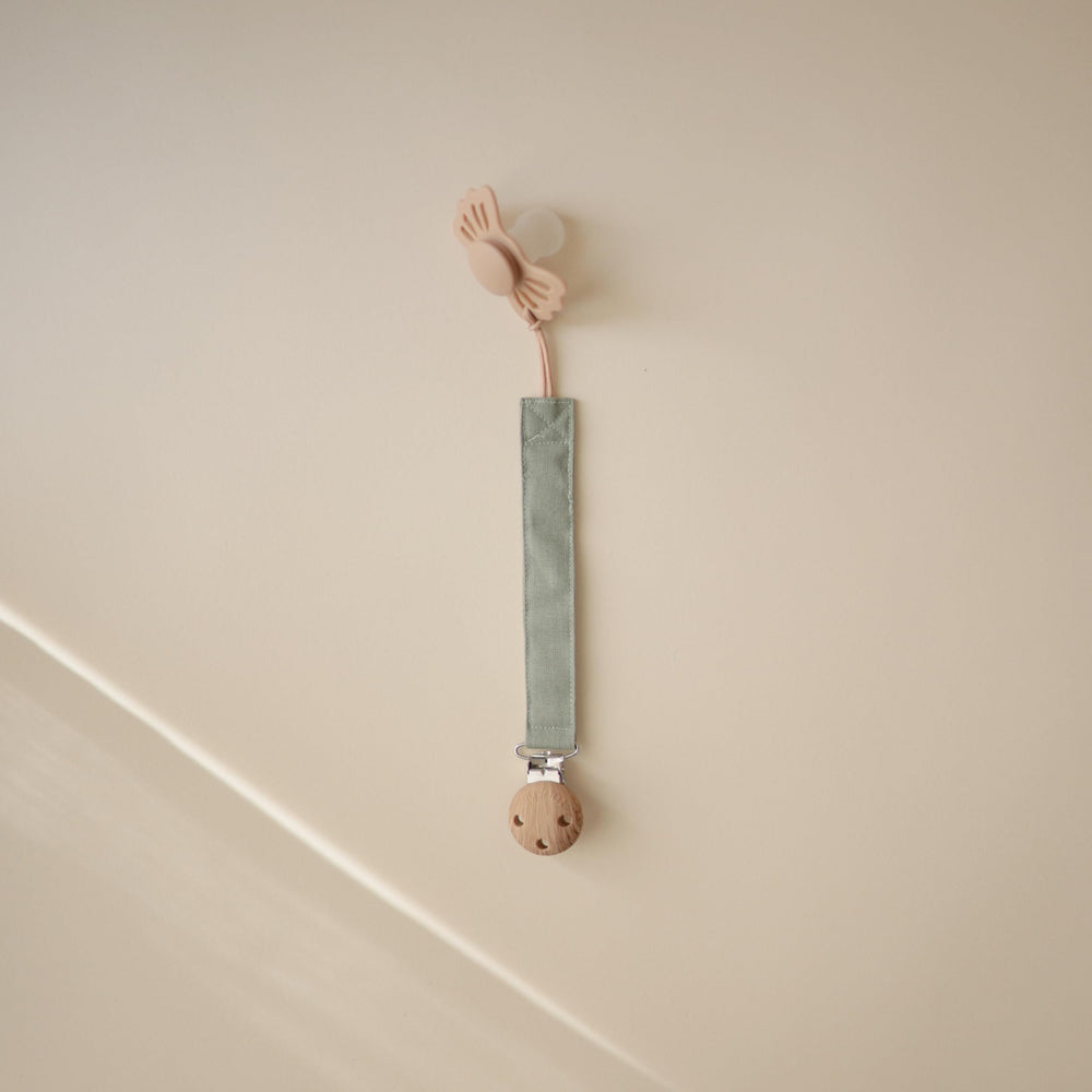 Mushie pacifier clip soft fabric strap on olive demonstrates gentle touch for baby comfort