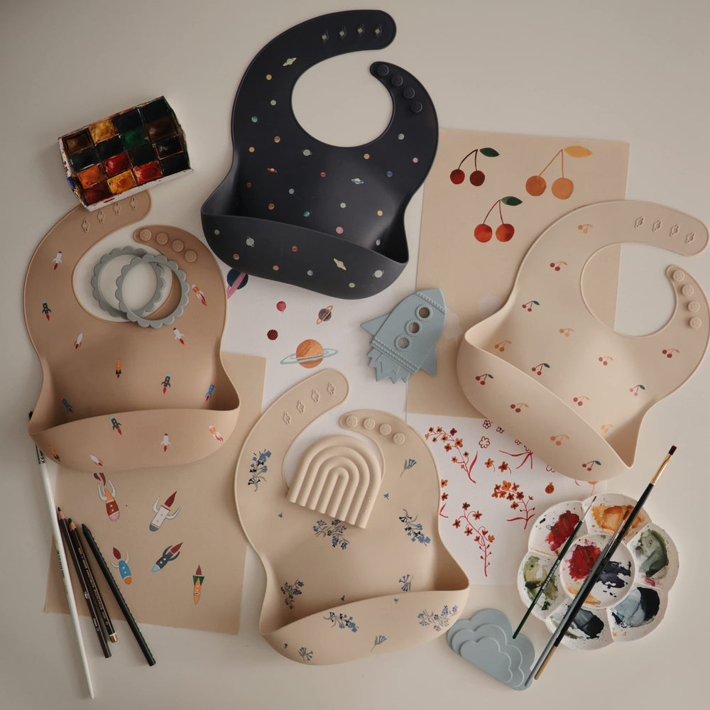 Mushie rocket ship bib flatlay displays surface texture and color