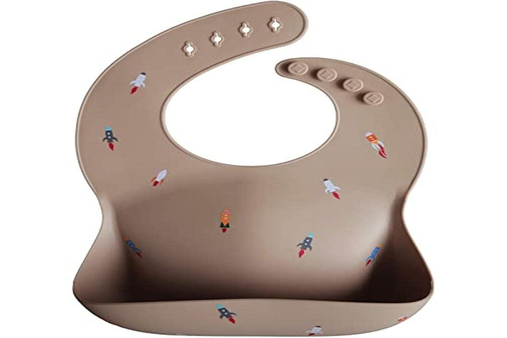 Mushie rocket ship bib worn on baby illustrates flexible, comfy silicone
