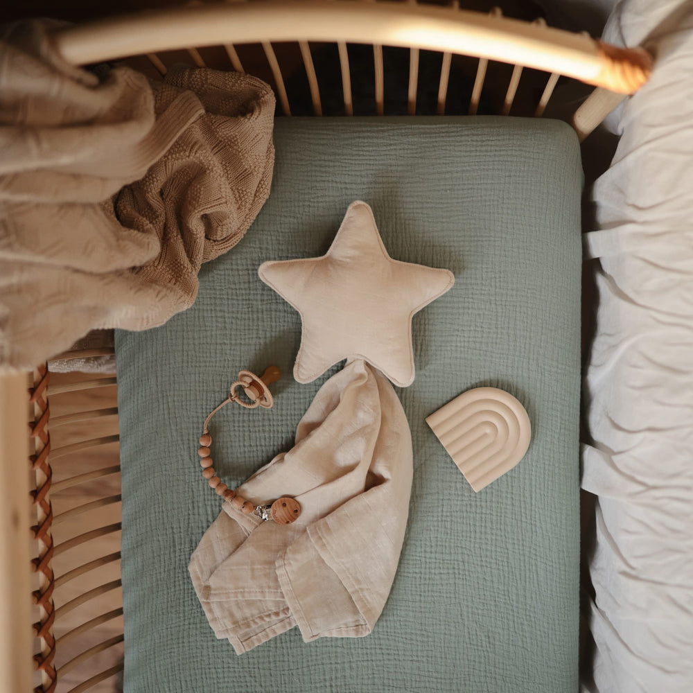 Mushie roman green crib sheet folded to show deep pocket fit and snug elastic.