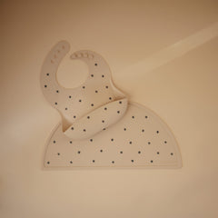 Mushie Black Daisy bib front pocket catches crumbs to keep feeding area tidy.