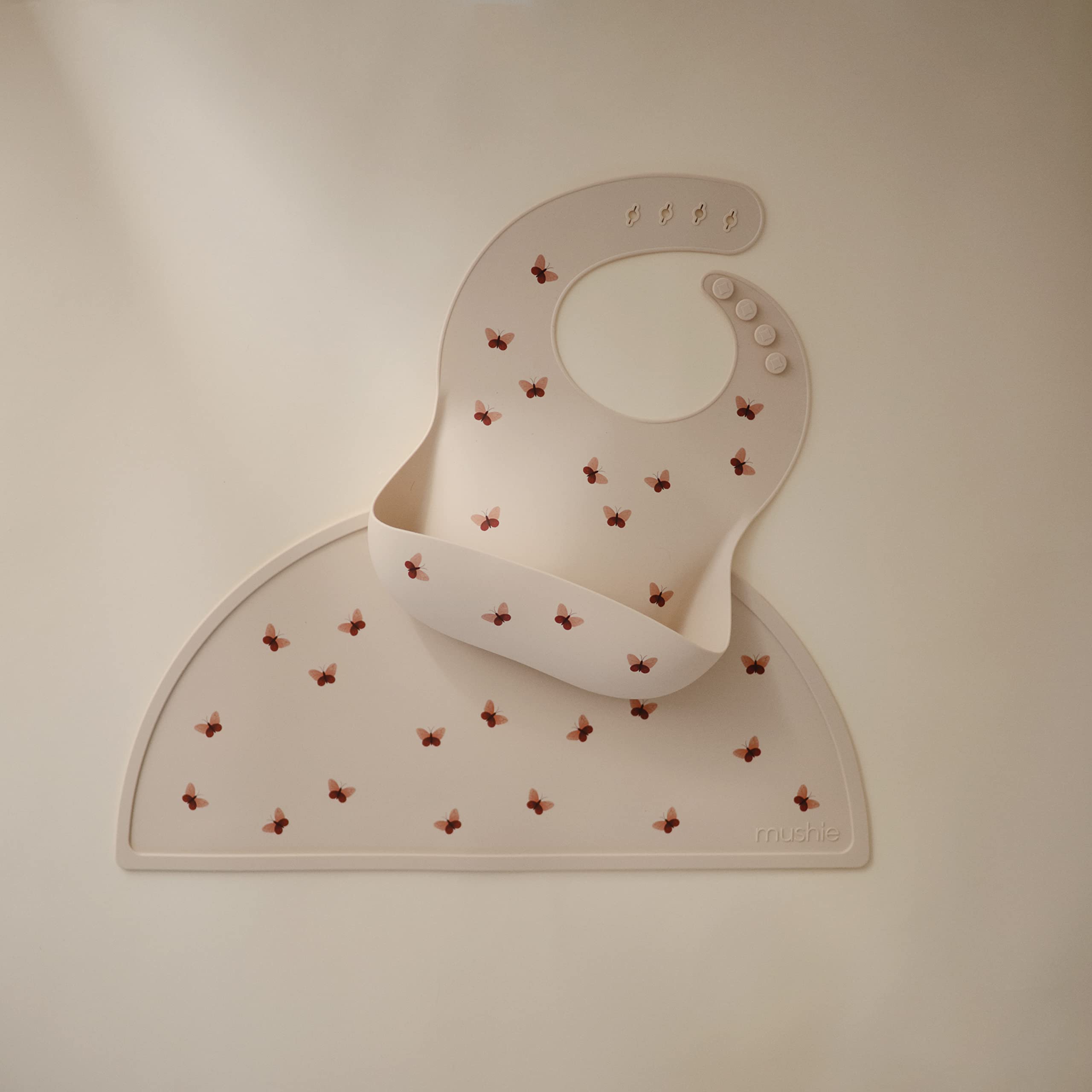 Mushie silicone bib butterflies worn by baby demonstrates adjustable neck for a snug fit