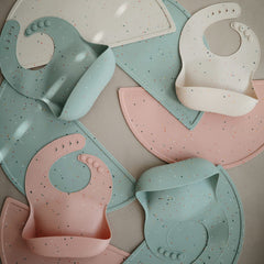 Mushie bib deep front pocket keeps crumbs off surfaces during feeding.