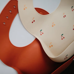 Mushie silicone bib deep-pocket cherries catching food during meals.