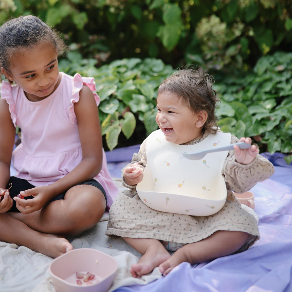 Mushie silicone bib in use during feeding with tray and mats.