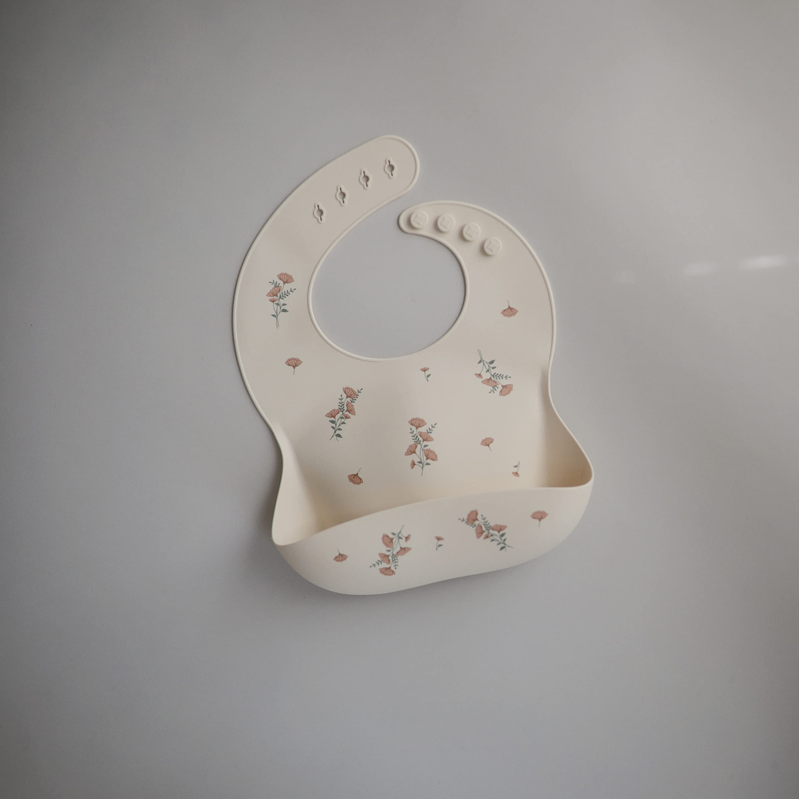 Mushie pink flowers bib close-up shows adjustable neck fastener for comfy fit