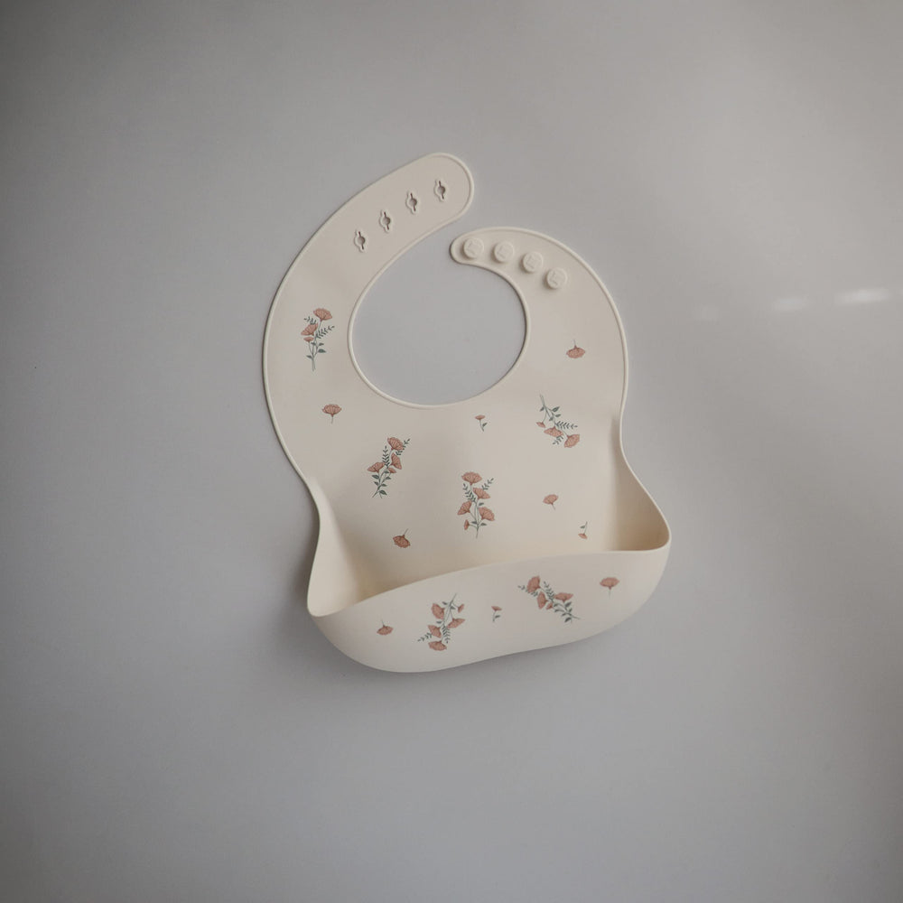 Mushie pink flowers bib close-up shows adjustable neck fastener for comfy fit