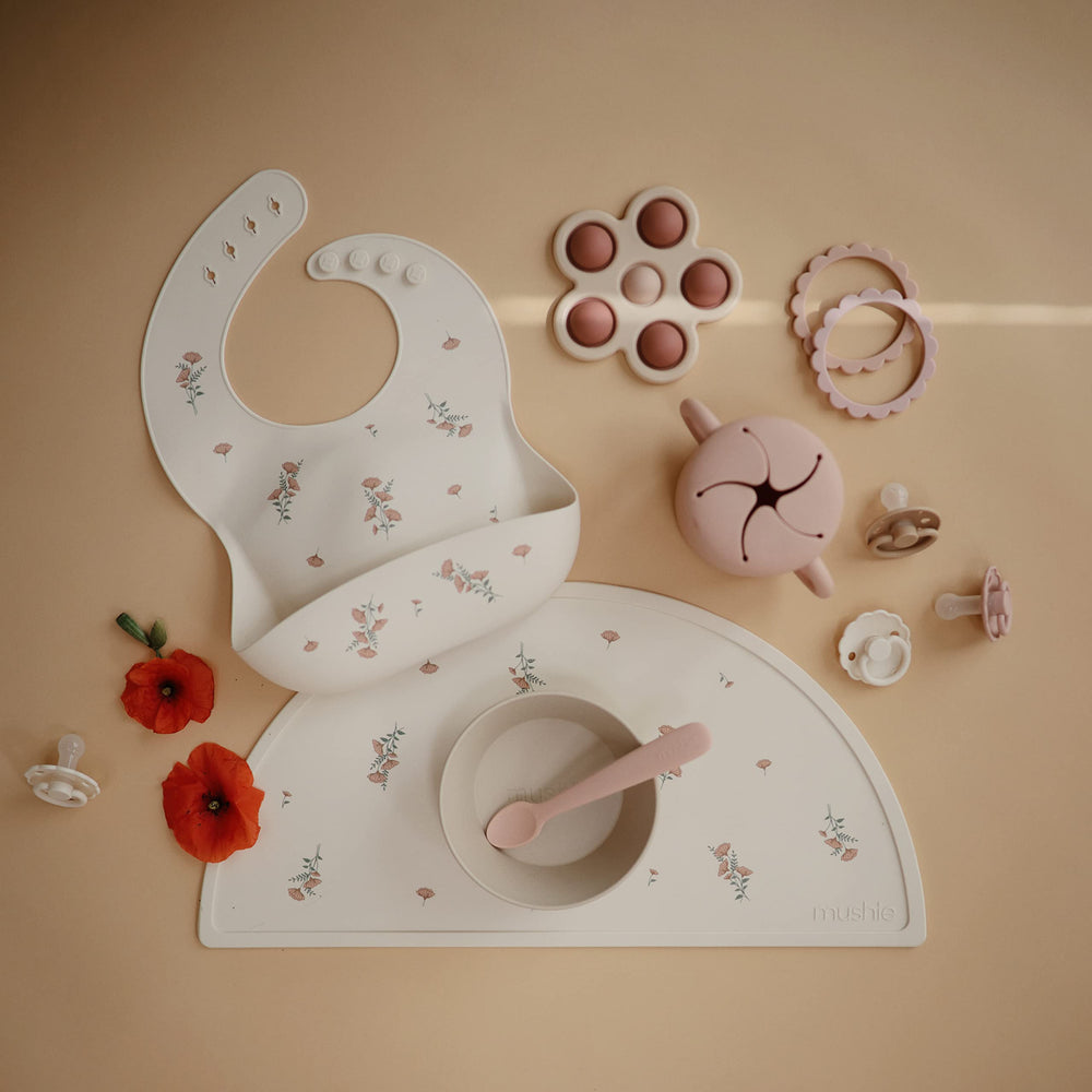 Mushie pink flowers bib on high chair tray during family meals