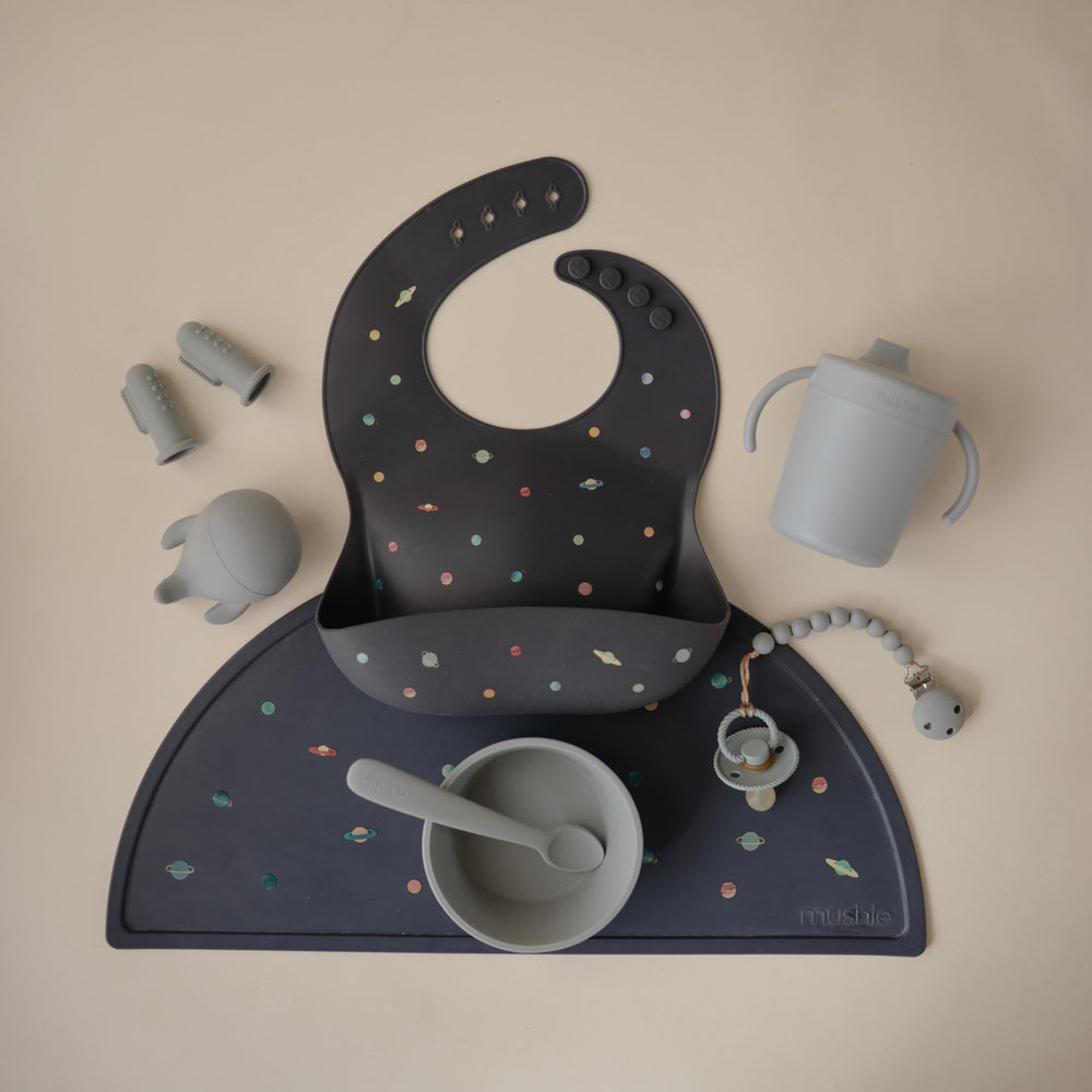 Mushie Planets bib pocket catching crumbs to keep meals mess-free.