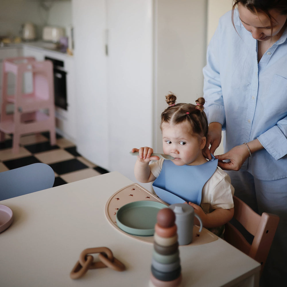 Mushie powder blue deep-pocket bib on table demonstrates easy mess containment