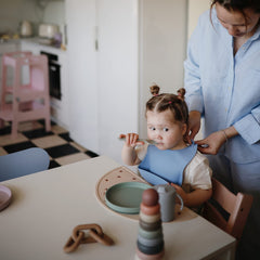 Mushie powder blue deep-pocket bib on table demonstrates easy mess containment
