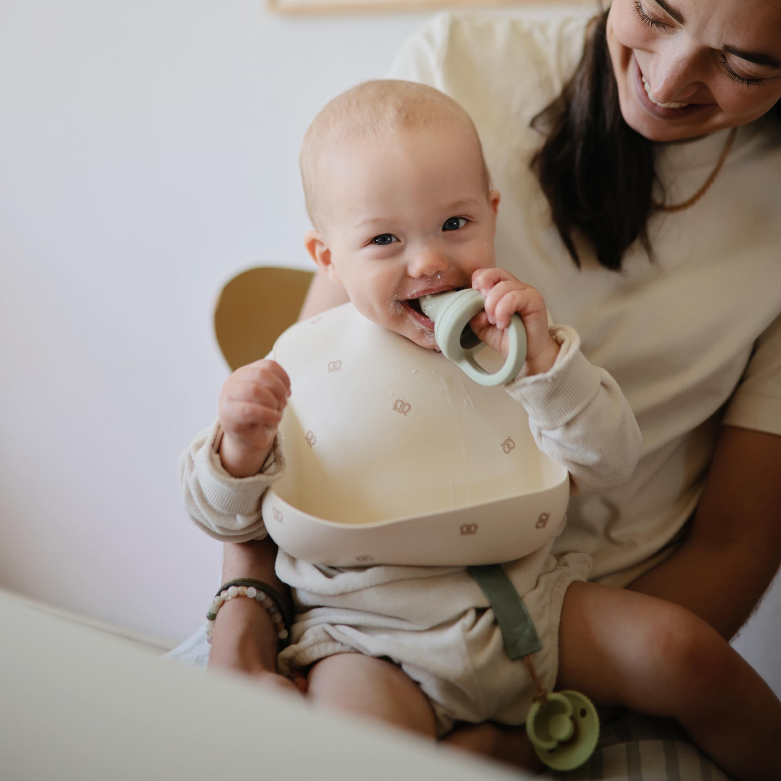 Mushie silicone baby bib Pretzel cleaning action shows quick soap wash and air-dry.