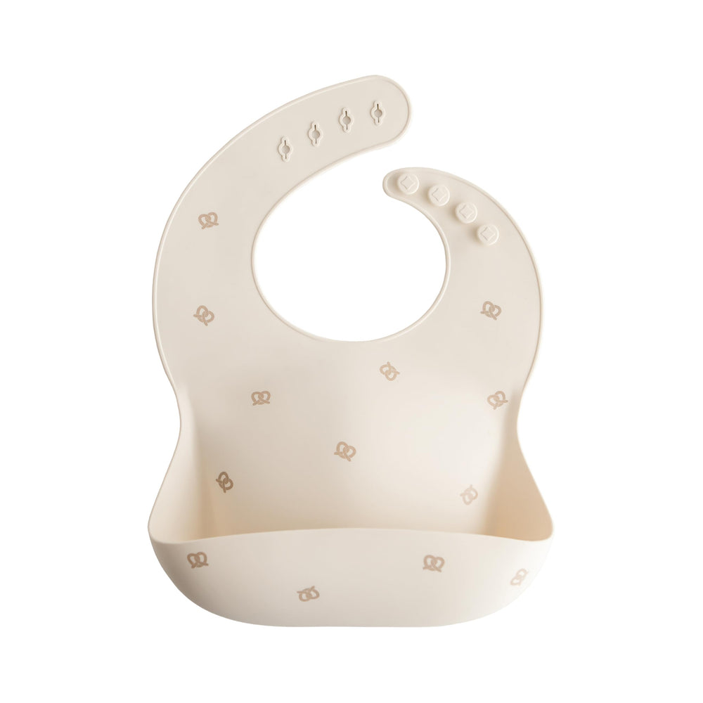 Mushie silicone baby bib Pretzel pattern with open pocket for catching crumbs during meals.