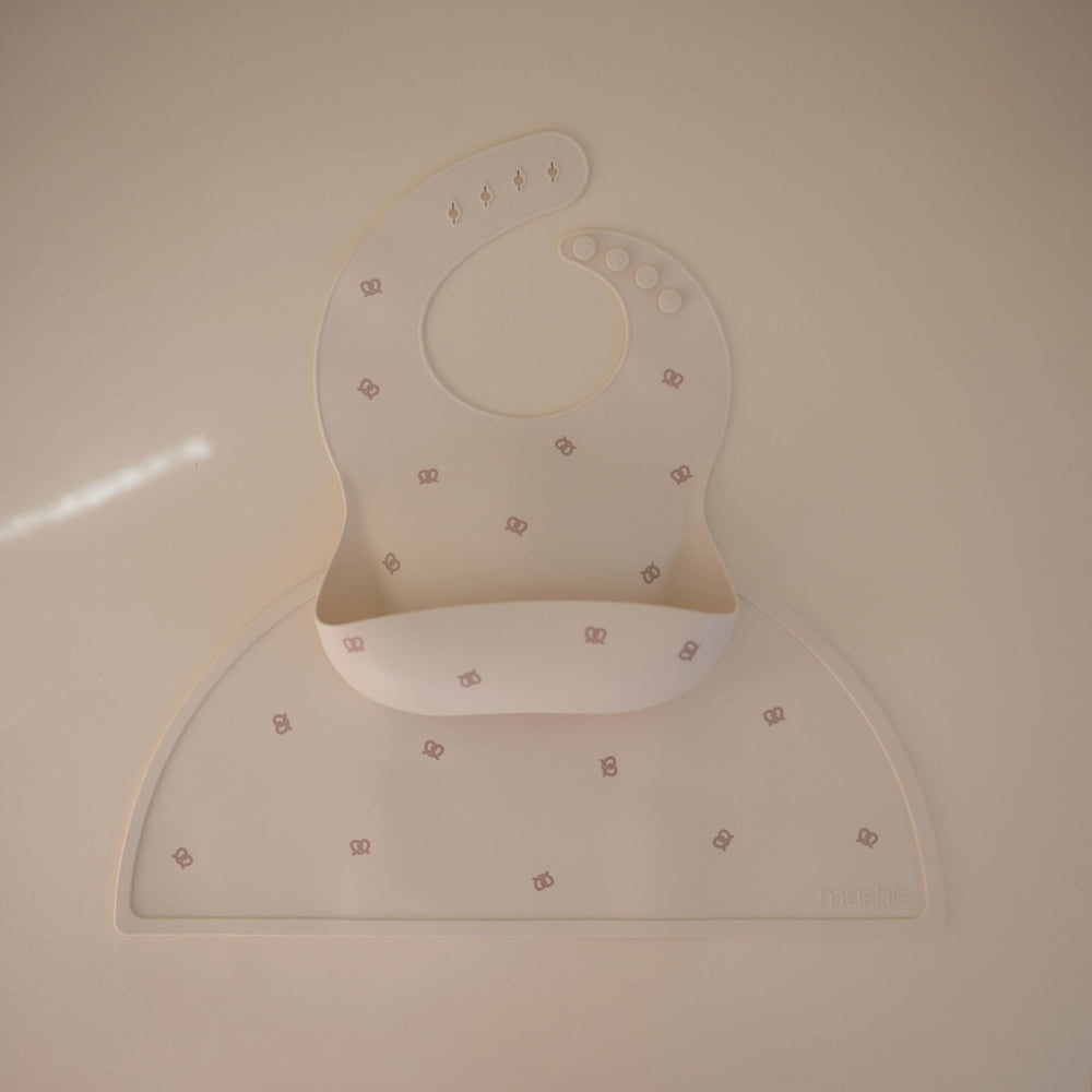 Mushie silicone baby bib Pretzel pocket full ready to catch spills.