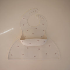 Mushie silicone baby bib Pretzel pocket full ready to catch spills.