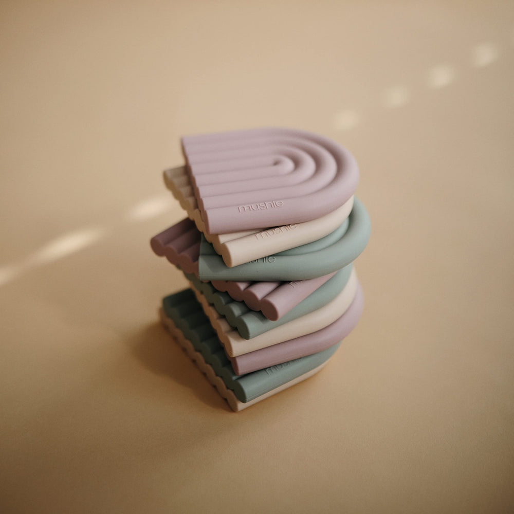Mushie rainbow teether held by baby hands for calming relief