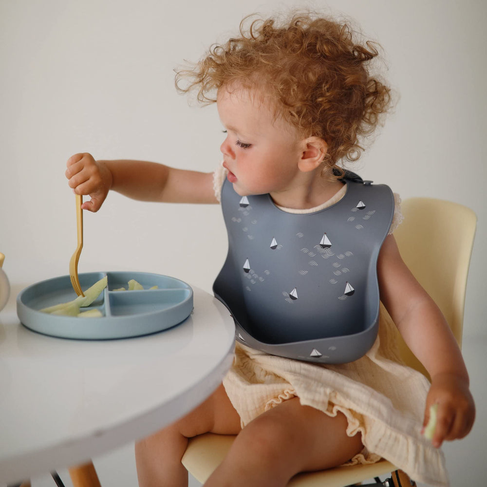Mushie silicone bib front pocket catches crumbs, reducing mess at each bite.