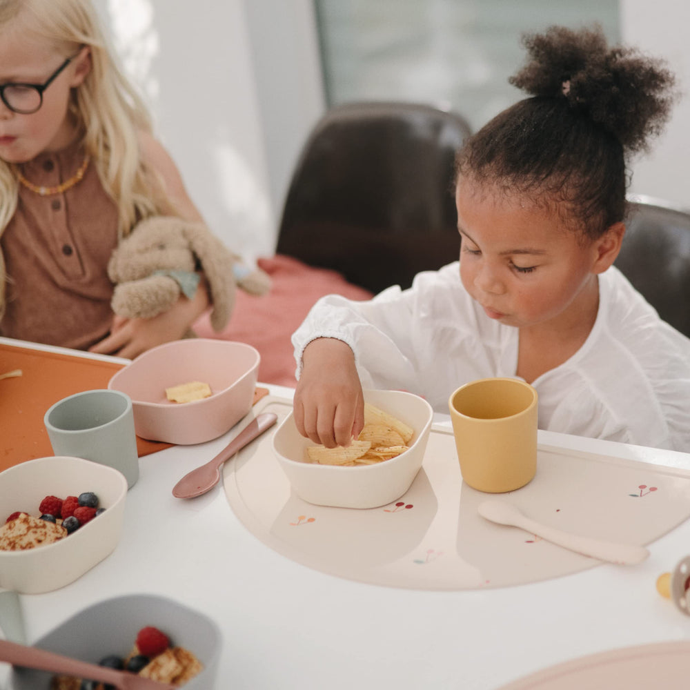 Mushie silicone placemat cherries flat lay with dinnerware to inspire coordinated mealtimes.