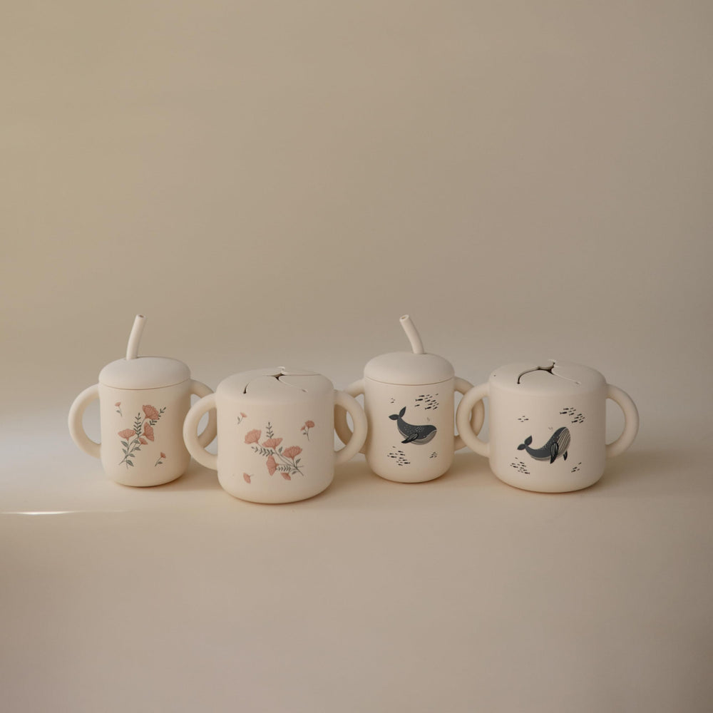 Mushie silicone snack cup whales in use on the go with snacks easily accessible.