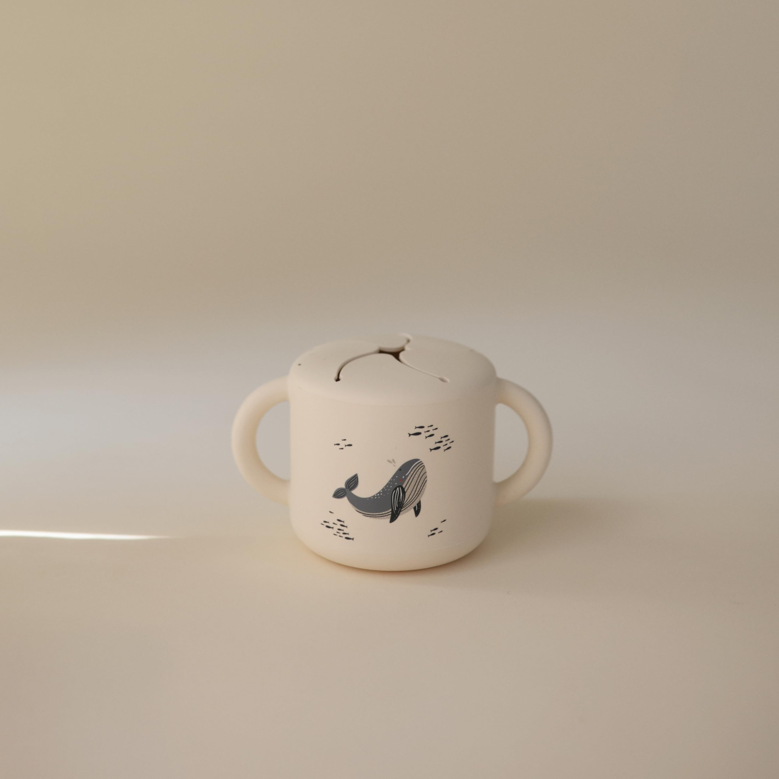 Mushie silicone snack cup whales close-up shows two handles for secure travel grip.