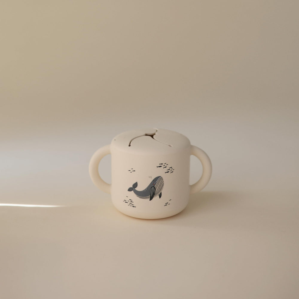Mushie silicone snack cup whales close-up shows two handles for secure travel grip.