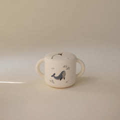 Mushie silicone snack cup whales close-up shows two handles for secure travel grip.